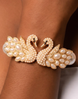 Anastasia statement bracelet shown on wrist with two sculptural pearl swans facing one another in a gold tone setting.