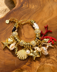 Statement charm bracelet featuring coral accents, starfish charms, seashell details, pearl embellishments, pavé crystal accents, and gold-tone hardware by Sassy Jones.