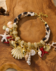 Statement charm necklace featuring pearl-studded shell pendants, coral accents, starfish charms, seashell details, pavé crystal elements, and gold-tone hardware by Sassy Jones.