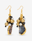 Chrysallis dangle earrings featuring irregular natural agate stones edged in gold with black and white bead accents. Sassy Jones natural agate earrings with textured stone drops, matte gold beads, and faceted black accents.
Black, white, and gold dangle earrings featuring clustered beads above natural raw edge agate slices.
Chrysallis Natural Black/Gold earrings featuring unique agate stone drops suspended beneath dimensional bead clusters.
