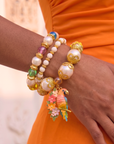 Three piece tropical bracelet stack featuring luminous pearls, colorful artisan beads, floral accents, butterfly charms, and a detailed tropical parrot charm in gold tone.