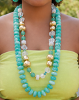 Turquoise statement necklace featuring layered rounded beads with clear, white and metallic gold colored details.