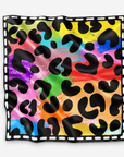A square scarf featuring a vibrant rainbow watercolor background overlaid with a black leopard print pattern, finished with a white dashed border on a light gray background.