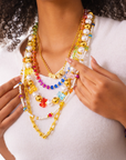 Colorful layered pearl and teddy bear necklace paired with a glittering rose gold lipstick clutch featuring three exclusive pink lipstick shades by Sassy Jones.