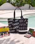 Vacation Escape Gift Set featuring the Sassy City Tote Black & White, Queen Luxe Scarf, Mojave Eyeshadow Palette, and Sunkissed Smooches 6pc Lip Gloss Set displayed poolside.