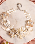 Mother of pearl floral statement necklace with sculptural petals and pearl clusters inspired by wisteria blossoms worn on a woman's neckline