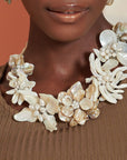 Mother of pearl floral statement necklace with sculptural petals and pearl clusters inspired by wisteria blossoms worn on a woman's neckline
