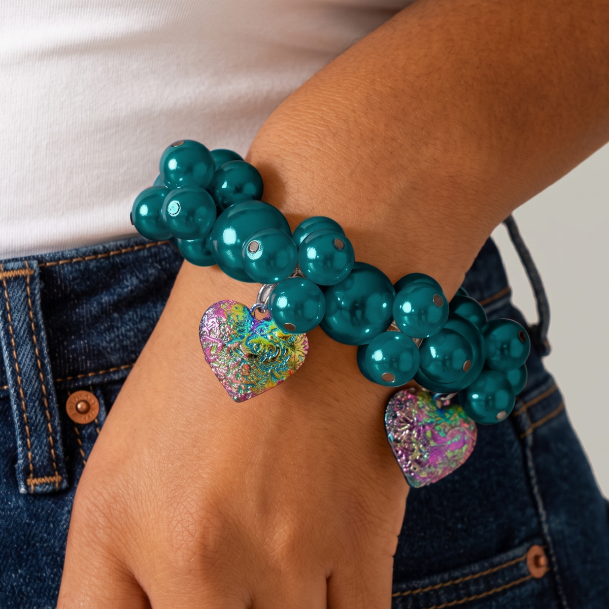 Amora Rainbow Teal stretch bracelet shown on wrist with mixed size teal glass pearls and dangling heart charms.