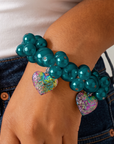 Amora Rainbow Teal stretch bracelet shown on wrist with mixed size teal glass pearls and dangling heart charms.
