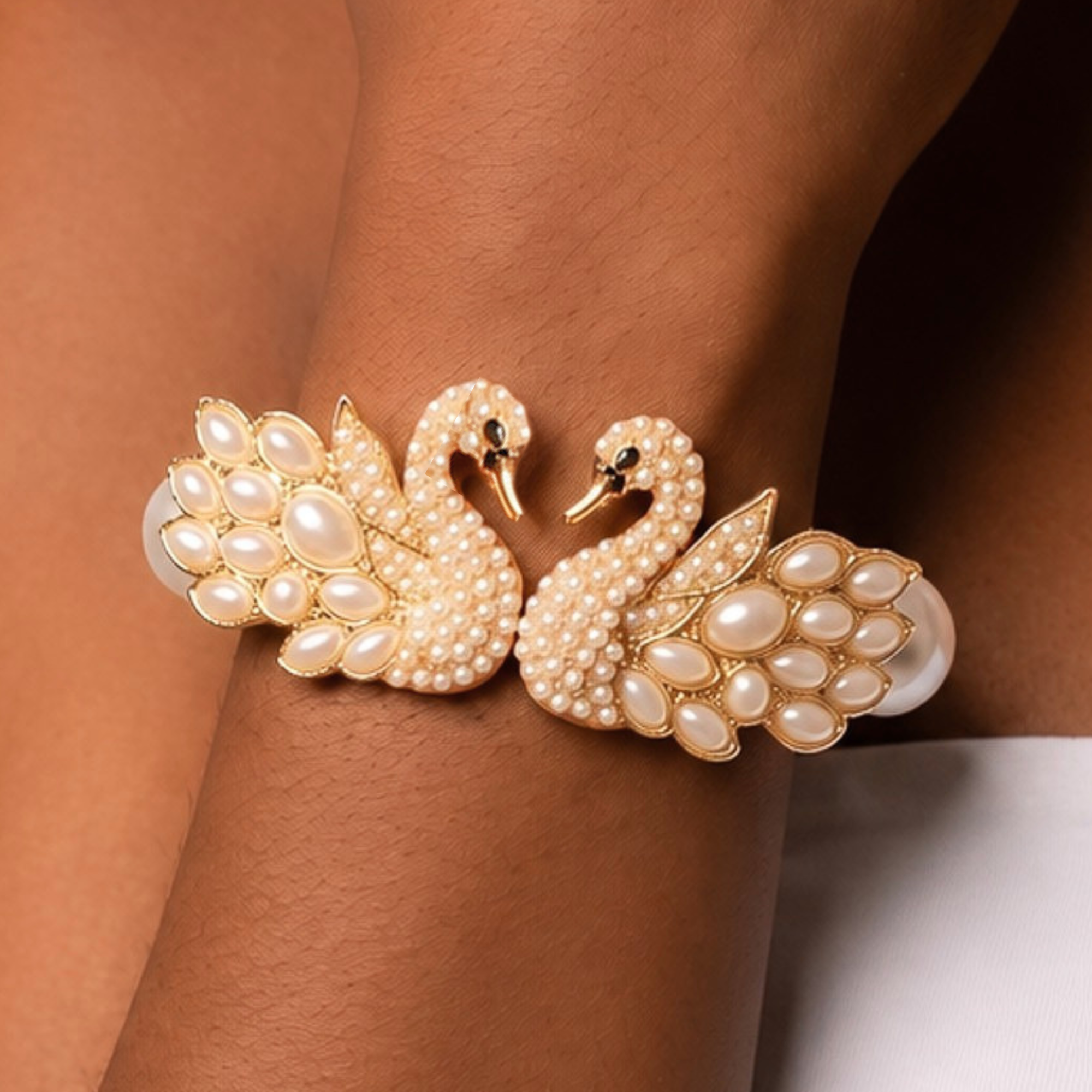 Anastasia statement bracelet shown on wrist with two sculptural pearl swans facing one another in a gold tone setting.