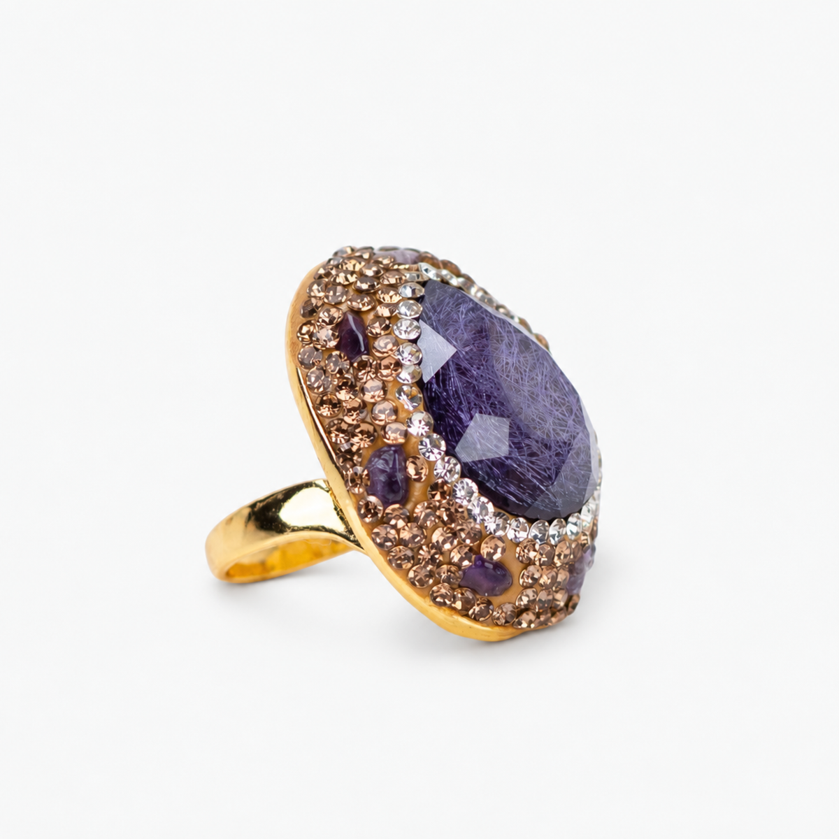 Purple statement ring featuring a faceted stone surrounded by crystals and textured Gold tone finish details.