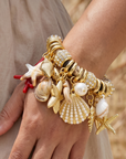 Statement charm bracelet featuring coral accents, starfish charms, seashell details, pearl embellishments, pavé crystal accents, and gold-tone hardware by Sassy Jones.