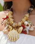 Statement charm necklace featuring pearl-studded shell pendants, coral accents, starfish charms, seashell details, pavé crystal elements, and gold-tone hardware by Sassy Jones.