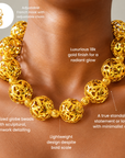 Gold statement necklace featuring large hollow globes with intricate sculptural cutout detailing.