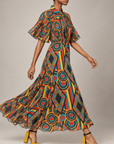 Full length view of the Imani Afrikaan dress with pleated flutter sleeves and a bold red, turquoise, yellow, orange, and black print.