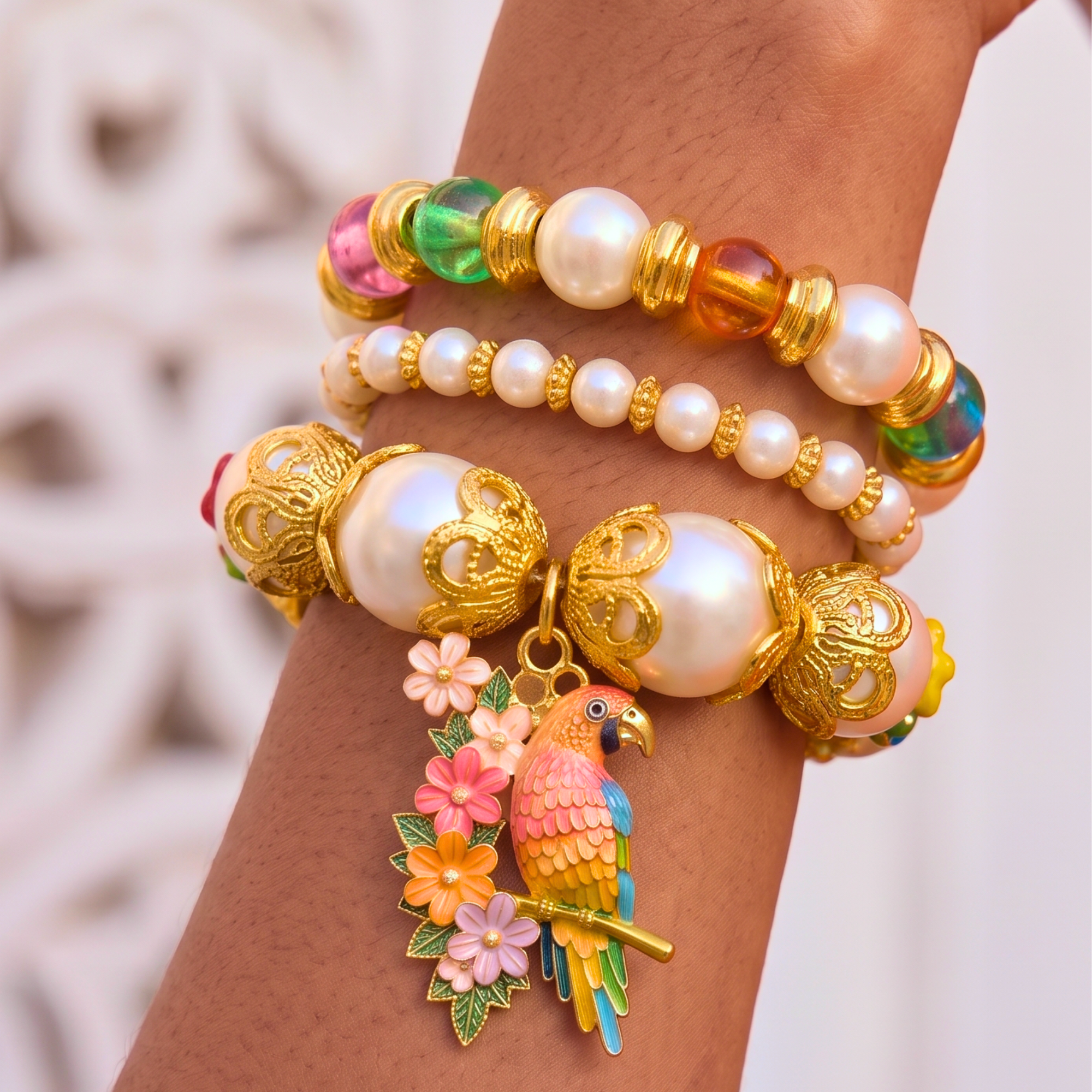 Three piece tropical bracelet stack featuring luminous pearls, colorful artisan beads, floral accents, butterfly charms, and a detailed tropical parrot charm in gold tone.