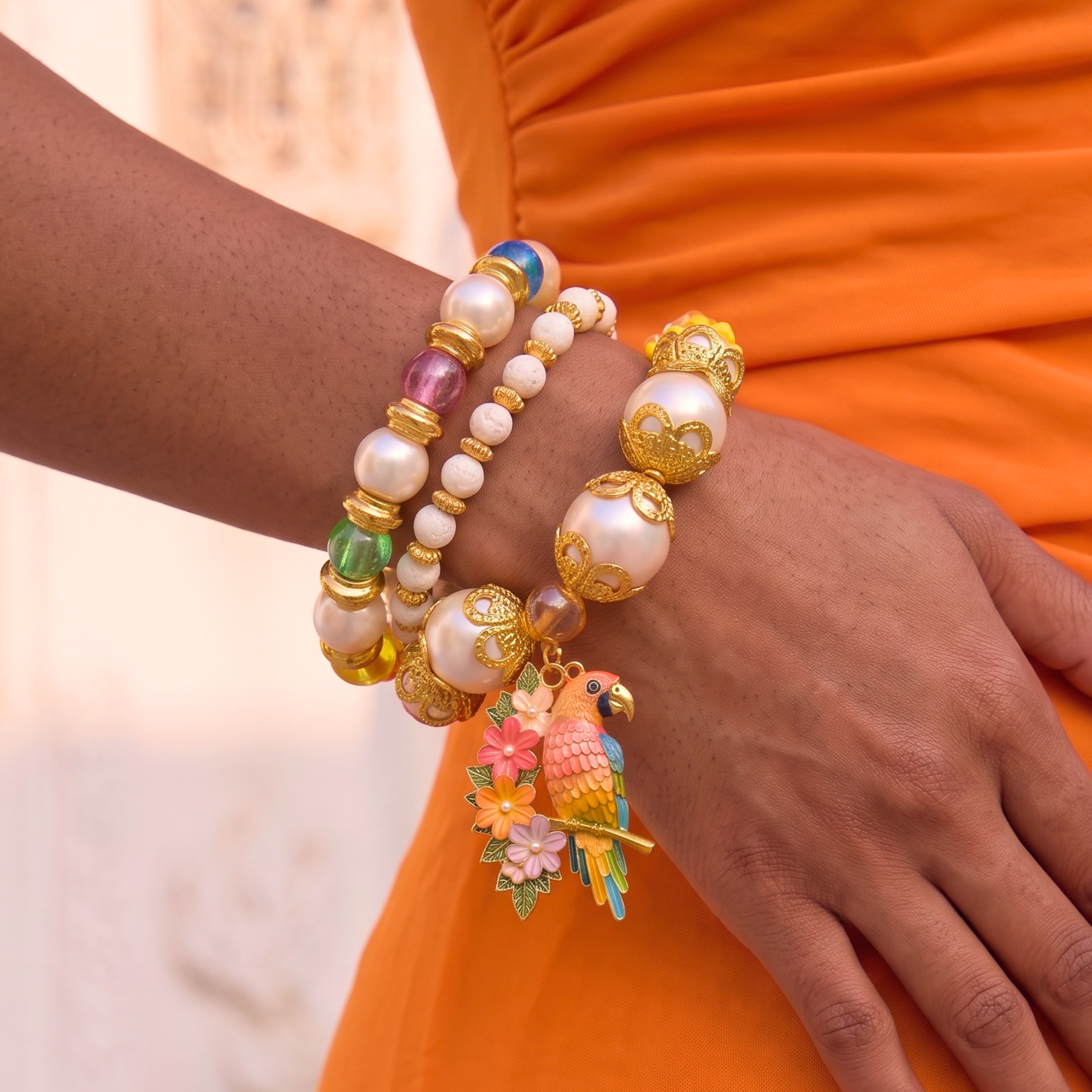 Three piece tropical bracelet stack featuring luminous pearls, colorful artisan beads, floral accents, butterfly charms, and a detailed tropical parrot charm in gold tone.