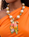 Colorful tropical statement necklace featuring luminous pearls, vibrant floral accents, artisan glass beads, and a detailed pink and gold parrot pendant.