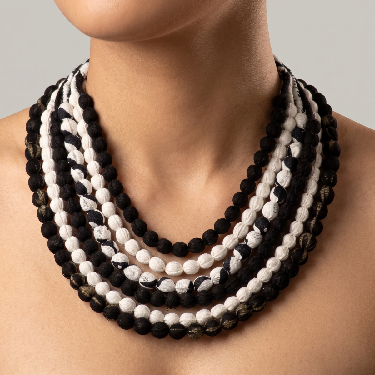 Multistrand black and white bib necklace featuring rounded cloth beads and adjustable fabric ties.