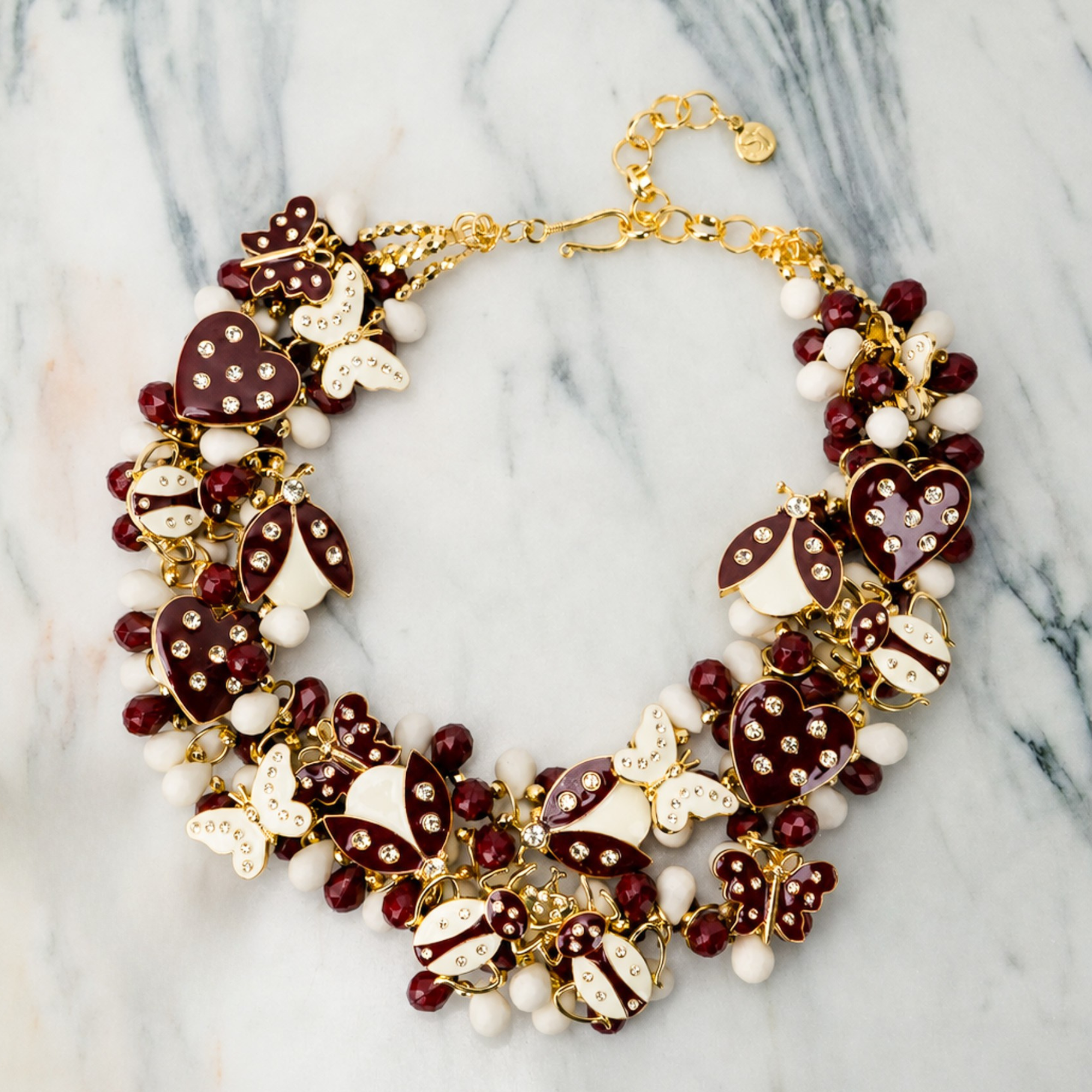 Crimson and cream statement bib necklace featuring removable butterfly, ladybug, and heart brooch charms with 18K gold-plated accents and faceted bead details.