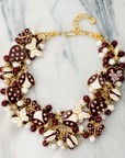 Crimson and cream statement bib necklace featuring removable butterfly, ladybug, and heart brooch charms with 18K gold-plated accents and faceted bead details.