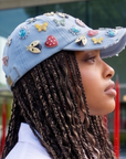 Light wash distressed denim ballcap featuring removable butterfly, ladybug, heart, and floral crystal brooch pins by Sassy Jones.