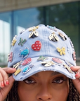 Light wash distressed denim ballcap featuring removable butterfly, ladybug, heart, and floral crystal brooch pins by Sassy Jones.