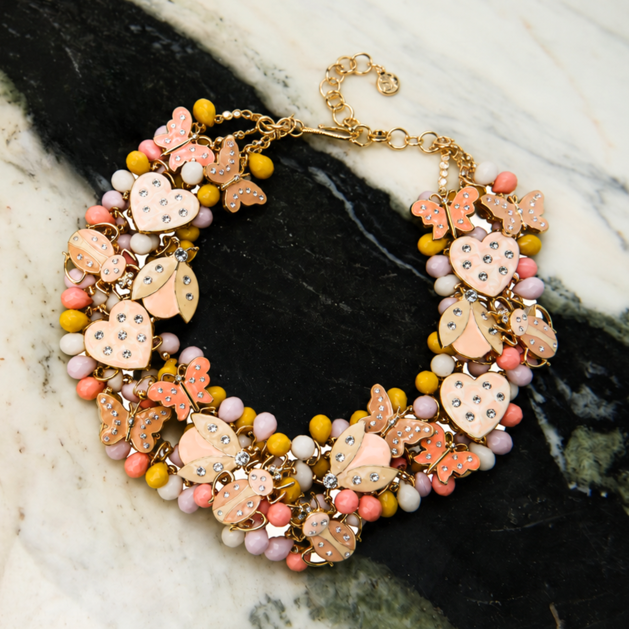 Peach and cream statement bib necklace featuring removable butterfly, ladybug, and heart brooch charms with 18K gold-plated accents and faceted bead details.