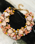 Peach and cream statement bib necklace featuring removable butterfly, ladybug, and heart brooch charms with 18K gold-plated accents and faceted bead details.