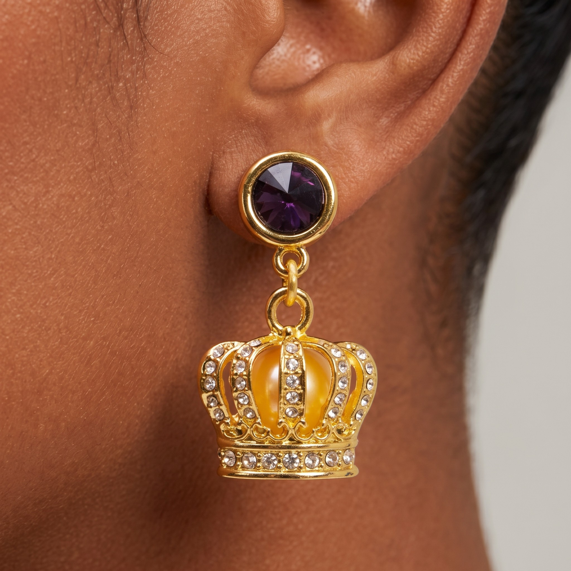 Close-up of Reign crown earring featuring purple gemstone-style stud and sparkling pavé details.