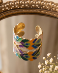 Statement cuff bracelet featuring hand painted enamel peacock feather motifs in vibrant jewel tones with gold tone detailing.