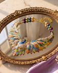 Statement peacock necklace featuring hand painted enamel feathers, multicolored crystal accents, gold tone detailing, and a sculptural peacock centerpiece.