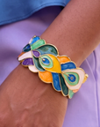 Statement cuff bracelet featuring hand painted enamel peacock feather motifs in vibrant jewel tones with gold tone detailing.