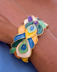 Statement cuff bracelet featuring hand painted enamel peacock feather motifs in vibrant jewel tones with gold tone detailing.