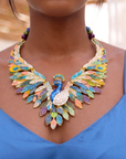 Statement peacock necklace featuring hand painted enamel feathers, multicolored crystal accents, gold tone detailing, and a sculptural peacock centerpiece.