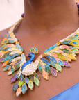 Statement peacock necklace featuring hand painted enamel feathers, multicolored crystal accents, gold tone detailing, and a sculptural peacock centerpiece.