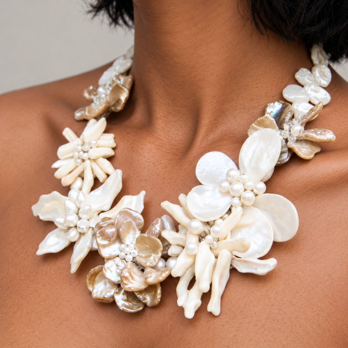 Mother of pearl floral statement necklace with sculptural petals and pearl clusters inspired by wisteria blossoms worn on a woman's neckline