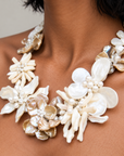 Mother of pearl floral statement necklace with sculptural petals and pearl clusters inspired by wisteria blossoms worn on a woman's neckline