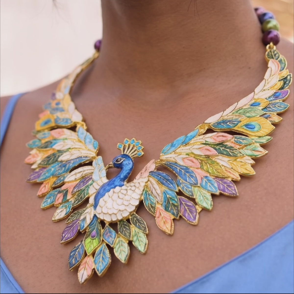 Sassy Jones peacock necklace shown on model featuring layered jewel toned feathers and gold tone finish.