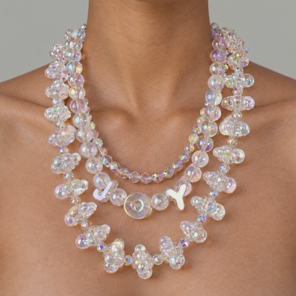 Close up of layered iridescent statement necklace with clustered bubble beads and a delicate faceted center strand.