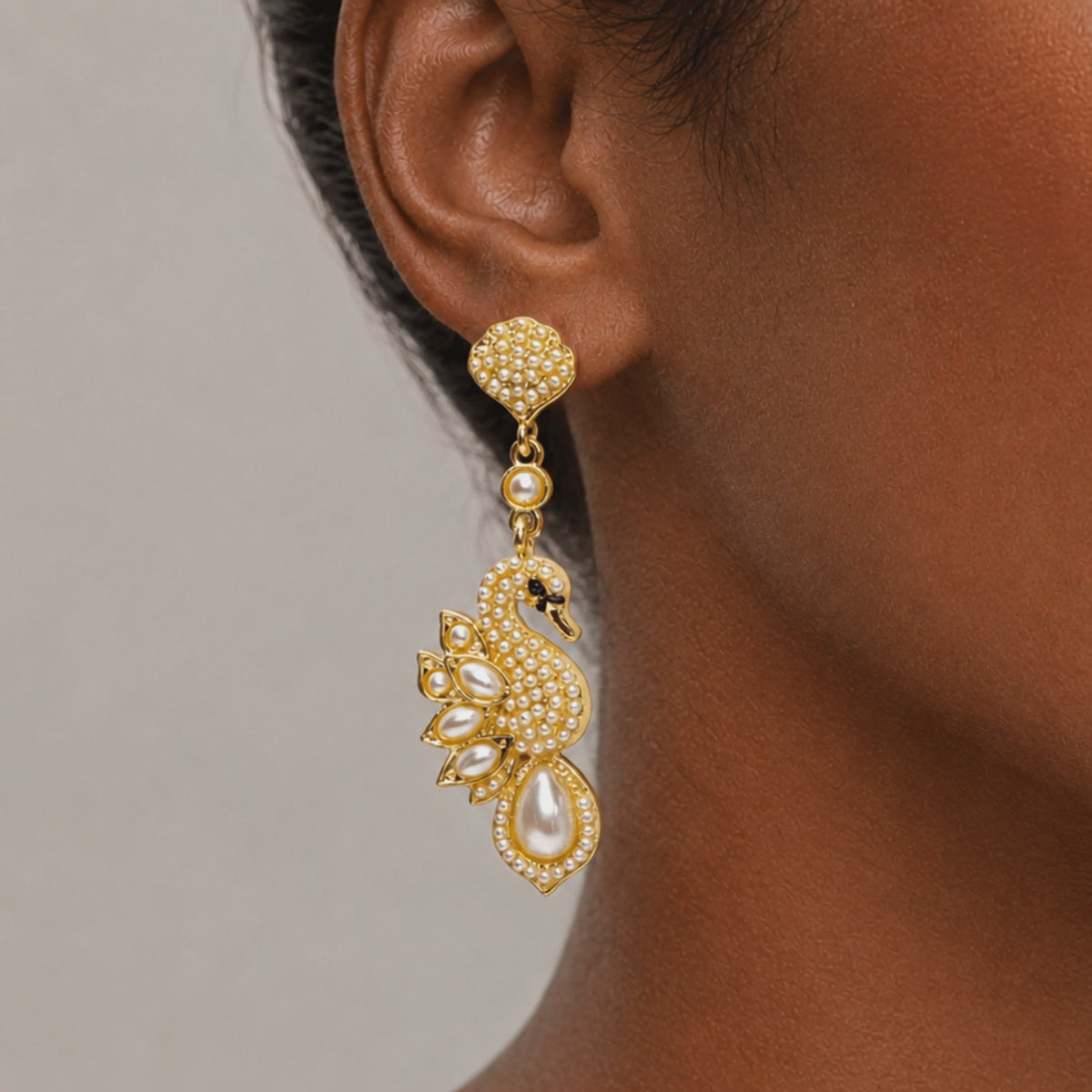 Elegant gold tone swan earrings designed with crystal covered bodies, layered pearl wings, and dangling teardrop pearls.
