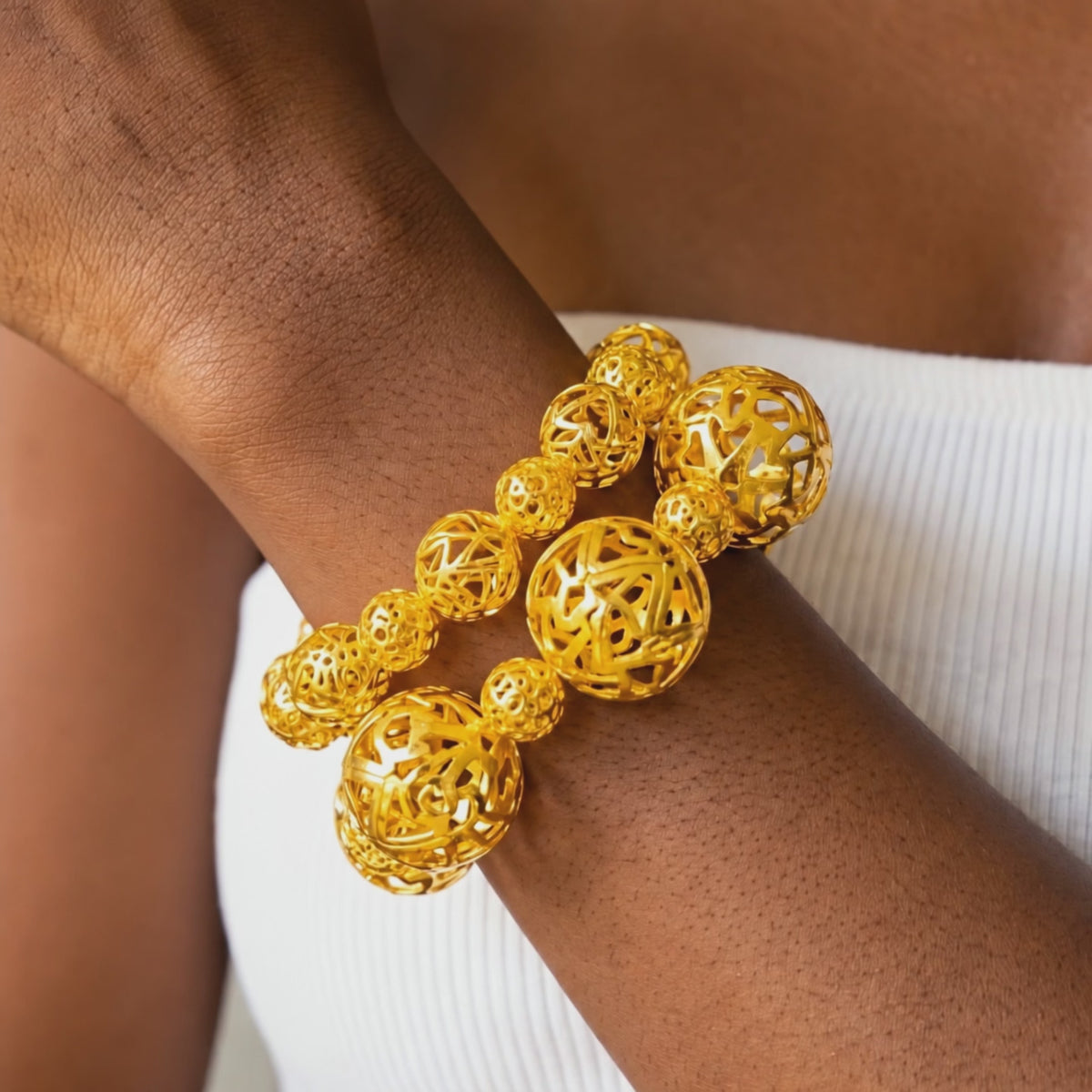 Close-up of gold stretch bracelets featuring intricate cutout sphere beads and dimensional textured details.