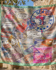 Close up of Charis Jetset Scarf showcasing a large blue New York stamp, colorful travel markings and vintage passport details.