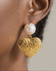 Romantic statement dangle earrings featuring ivory pearls and polished gold hearts with raised decorative texture.