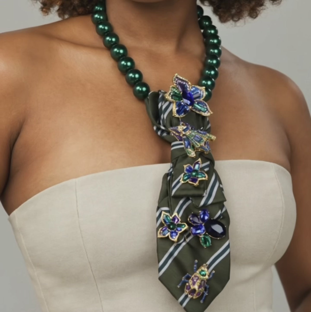 Close up of Valerie Miss Beasley necktie showcasing blue and green crystal flowers with ornate insect inspired brooches. 