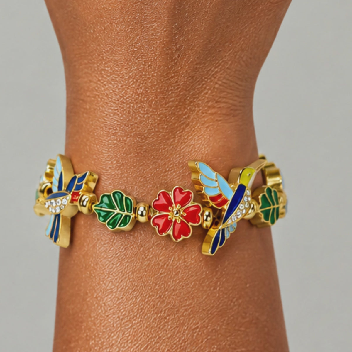 Close up of Cherish Hummingbird Bracelet highlighting blue wing detailing, sparkling crystal accents and colorful enamel flowers.