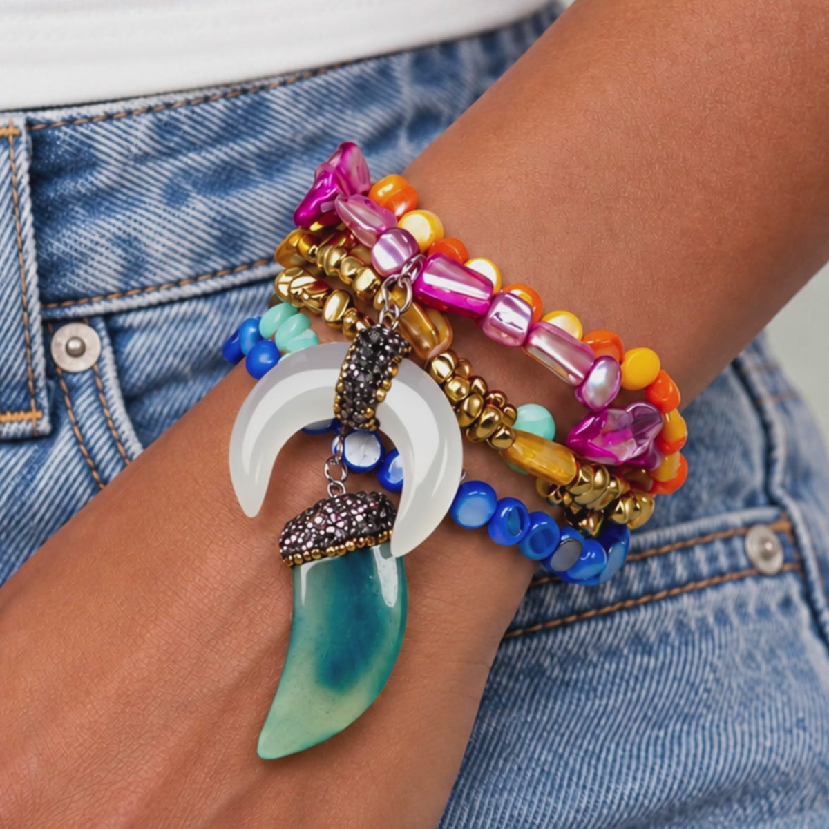 Close-up of Zuma five piece bracelet stack with colorful shell beads, golden hematite, chalcedony, and sculptural dangling charms.