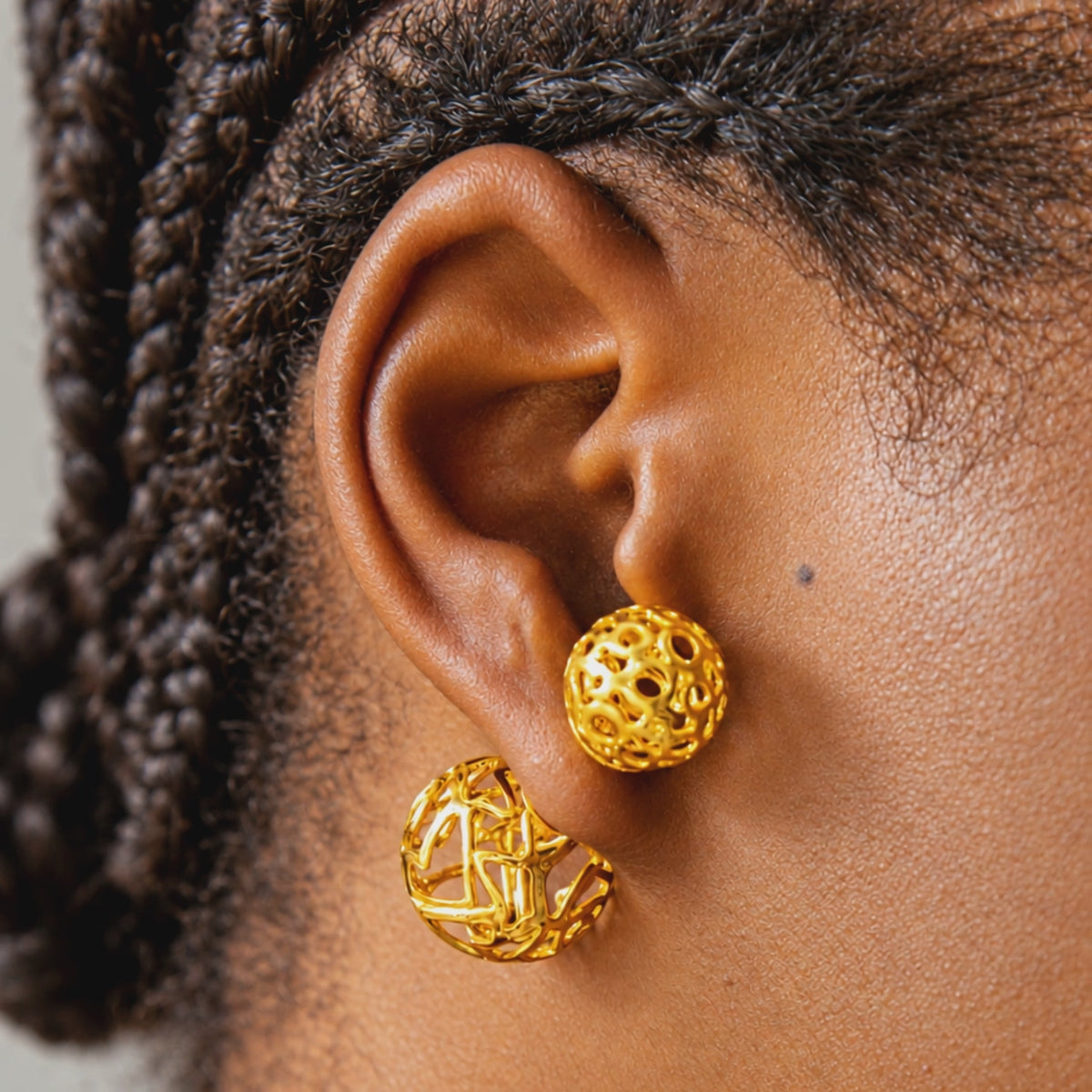 Gold statement stud earrings featuring a front and back double sphere silhouette with dimensional openwork texture.