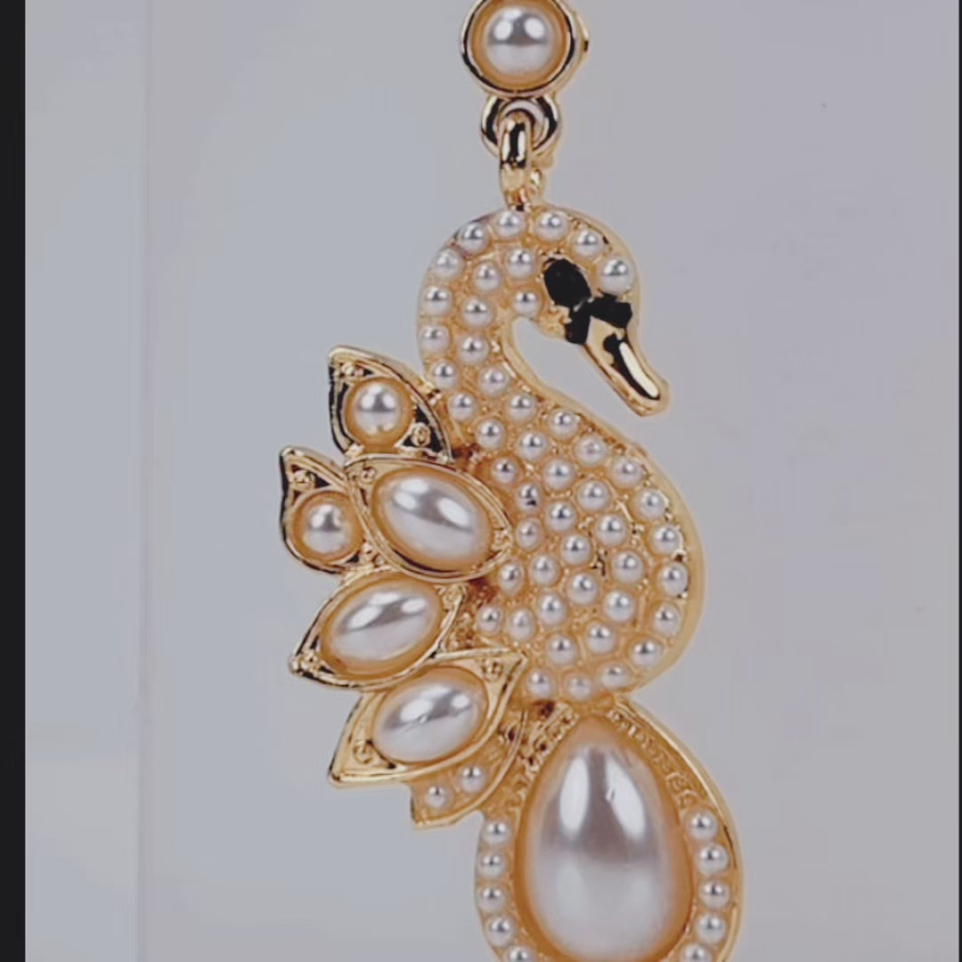 Elegant gold tone swan earrings designed with crystal covered bodies, layered pearl wings, and dangling teardrop pearls.
