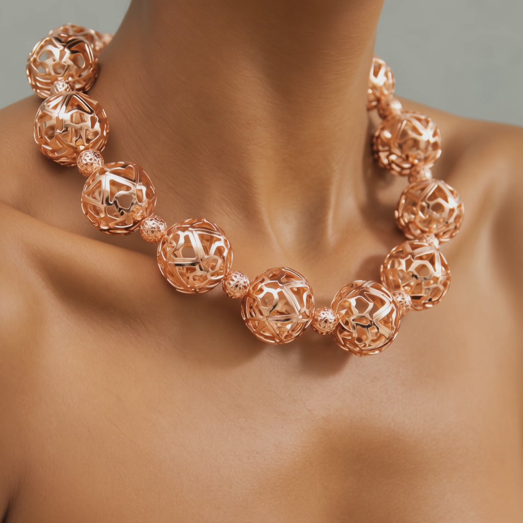 Close-up of sculptural rose gold necklace featuring alternating large openwork globes and petite textured beads.